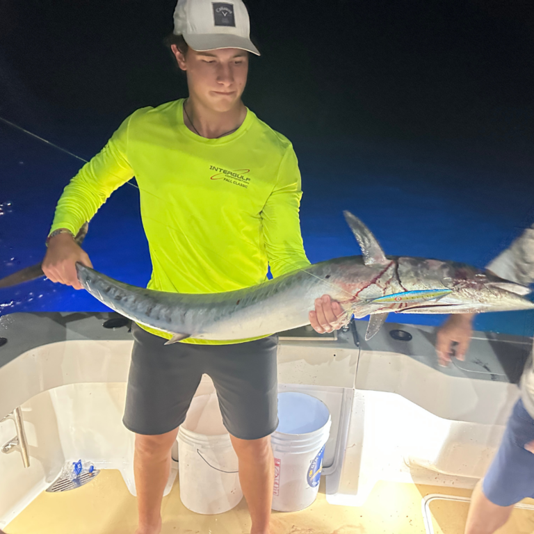 young man holding barracuda caught at night